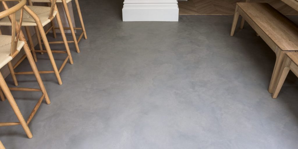 Light grey microcement floor in a modern dining area with natural wood furniture Light grey microcement floor in a modern dining area with natural wood furniture